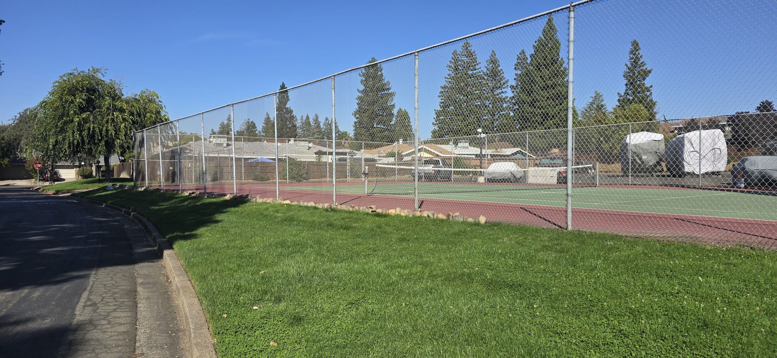Tennis court fence viewed from corner showing newly placed rock border